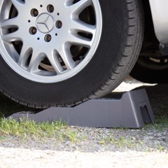 Ett däck vilar på en grå ramp med steg-design, som ger höjd och stabilitet på grus och gräs.